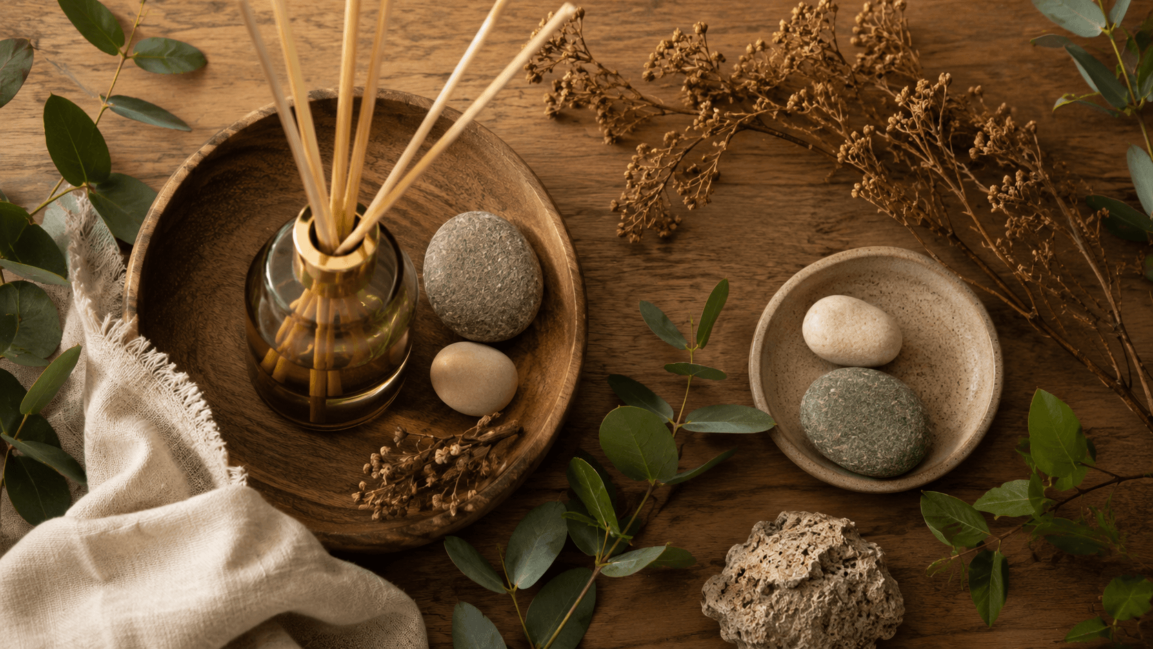 Close em difusor de aromas, pedras naturais, galhos e folhagens sobre superfície de madeira — detalhes sensoriais biofílicos