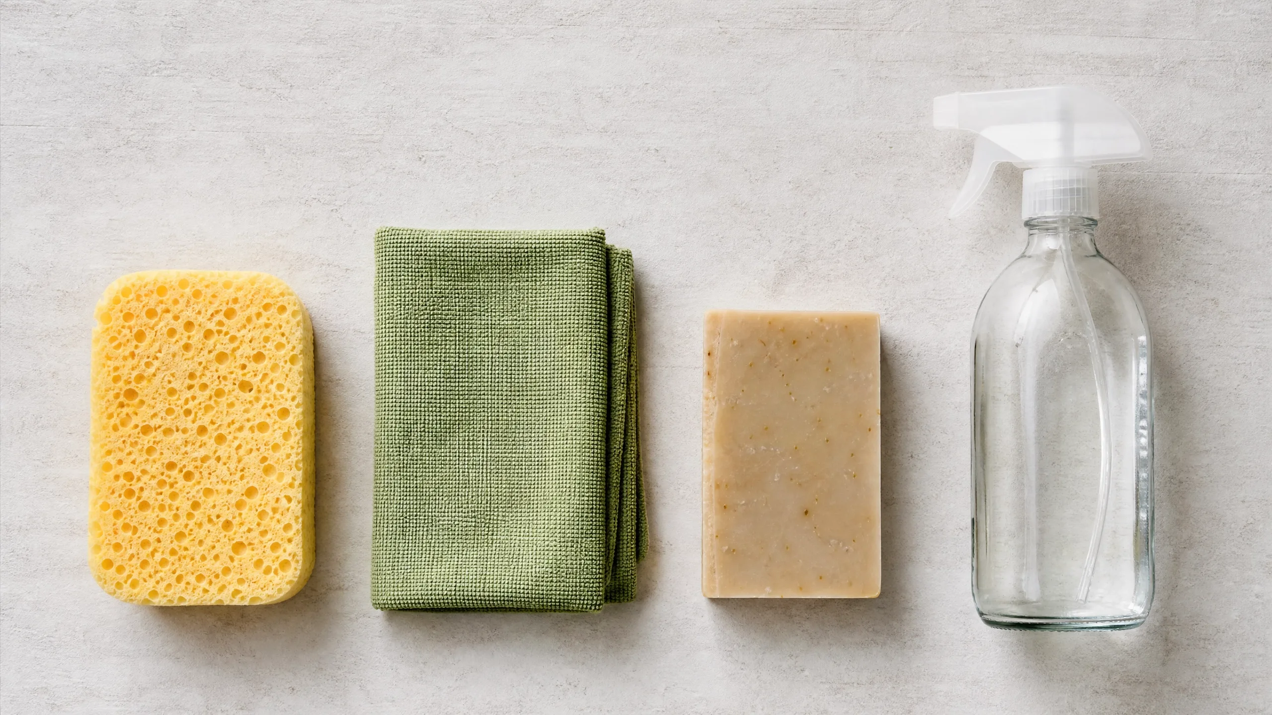 Flat lay com esponja de celulose, pano de microfibra, sabão ecológico e spray reutilizável
